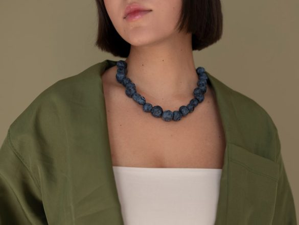 Femme portant un collier bleu pierre sur haut blanc et veste verte, design semblable aux discrets colliers espions