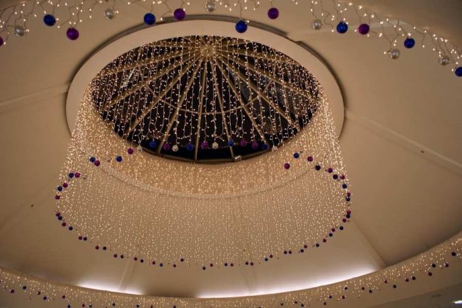 Plafond circulaire spectaculaire habillé de milliers de guirlandes lumineuses dorées et de boules colorées bleues et violettes en cascade, pour une décoration de plafond féerique.