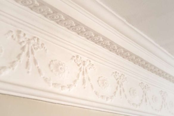 Gros plan sur une corniche en plâtre blanc finement sculptée de motifs floraux et de guirlandes en relief, solution classique et élégante pour habiller son plafond.