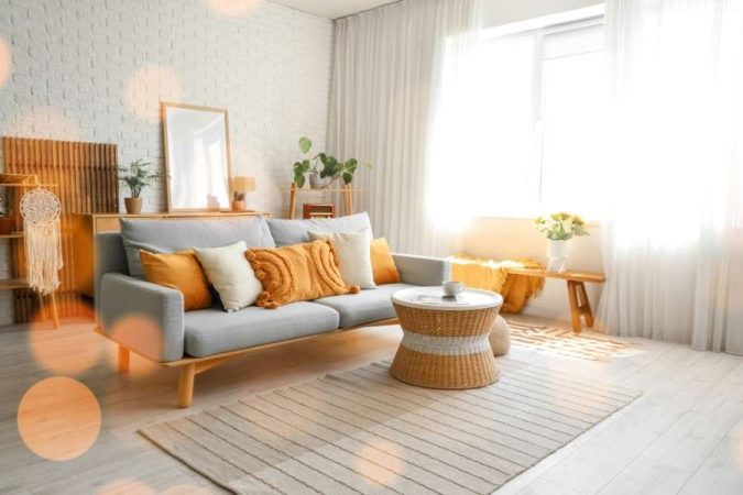 Un salon lumineux et bohème avec un canapé gris, des coussins ocre et une table basse en rotin pour moderniser son salon avec des matériaux naturels.
