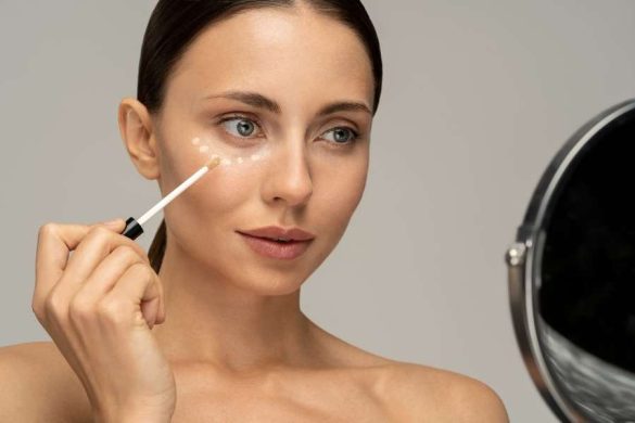 Une femme se regarde dans un miroir tout en appliquant des points de produit sur son visage avec un correcteur anti-cernes.